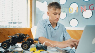 Akıllı öğrenci dizüstü bilgisayarla çalışırken araba modelini analiz ediyor. Bilgisayar kullanan mutlu liseli çocuk elektronik aletli masada robot model yapısını öğreniyor ya da öğreniyor. Öğretim.