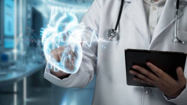 Tablet tutan yetenekli doktorlara yakın çekim yapın ve bulanık bir geçmişi olan kalp hologramına işaret edin. Tıp çalışanı teknolojiyi kullanarak tıbbi verileri kontrol ediyor ve analiz ediyor. İyileştirici.