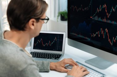 Bilgisayar ve dizüstü bilgisayarı kullanarak, çalışma masasındaki dinamik artırılmış borsa grafiğinin en yüksek kar değerini araştıran bir tüccar, modern ofisteki ekrandaki döviz kuru değerini analiz ediyor. Bireysel.