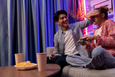 Oyun oynayan mutlu çiftin oturduğu kanepe joystickle oyun oynuyordu. Önden atıştırmalıklar ve kazanmak için gözlerini kapayan içkiler, evdeki modern neon ışıklı oturma odasında eğlenceli bir şekilde meydan okumaydı. İnfobahn.