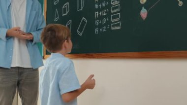 Düşük açılı kamera, yetenekli öğretmen çocuğa bakarken beyaz çocuğun tahtaya cevap yazdığını gösteriyor. Sorulara cevap vermek için gönüllü olan zeki ilkokul öğrencilerini kapatın. Eğitim. Pedagoji.