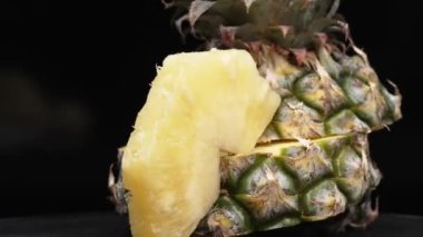 Taze ananaslı ve ayrı siyah arkaplanlı bir ananas dilimli videoyu kapat. Kaba ve balmumu kabuğu, dikenli yeşil yapraklardan bir taç, yemek fotoğrafçılığı. Geliştirilebilir.