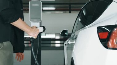 Yavaş çekim adamı, EV elektrikli arabasıyla alışveriş merkezinin otoparkına gidiyor. Şehrin sürdürülebilirlik yaşam tarzını yeşil, temiz, yeniden şarj edilebilir elektrikli araç iç organlarıyla şarj ediyor.