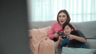 Annem kanepede yatarken, mutlu kız oyun oynuyor ve oturuyor. Beyaz bir ebeveyn ve çekici zeki bir kız elinde joystick ile birlikte vakit geçirip maç kazanmaya odaklanıyor. Yaşam tarzı. Pedagoji.