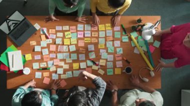 Akıllı iş adamlarının üst görüşü proje tasarımı hakkında toplantı odasında dizüstü bilgisayar ve yapışkan notlarla konuşur ve açıklar. Ayakta dururken logo tasarımının havadan görünüşü. Sempozyum.