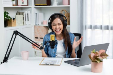 Sosyal medyada kulaklıkla canlı yayın yapan Asyalı sunucu modern stüdyoda yaşam koçluğu veya pazarlama dinleyicilerini selamlıyor. Taktik.