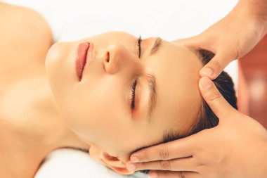 Yakın plan kadın stres önleyici kafa masajı yapmaktan ve lüks tatil beldesi veya otel spa salonundaki modern ışık ortamında yüz güzelliği eğlencelerini şımartmaktan zevk alıyor. Sessiz.