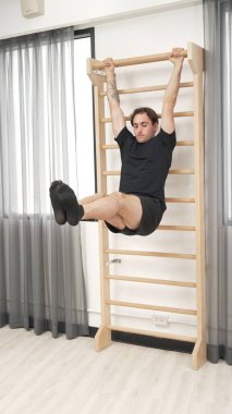 Asılı bacak egzersizi yapan mutlu bir adam vücut kaslarını güçlendirmek ve beden eğitimini iyileştirmek için duvar parmaklıkları üzerinde egzersiz yapıyor. Alt karın bölgesini iyileştirmek için erkek antrenör bacak yükseltme ameliyatı. Alışkanlık.