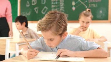 Çekici beyaz çocuk okulda matematik okurken kameraya bakıyor. Çeşitli şirin öğrenciler test yaparken öğretmen Asyalı çocuklara soru sorup tahtaya kağıt doğrultuyor. Pedagoji.