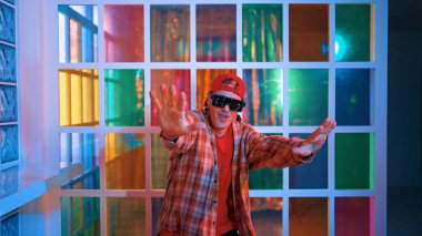 Komik break dansçı kameraya bakarken hiphop 'a doğru serbest adım atıyor. Çılgın mutlu hipster dans edip sokak dansı yaparken Led ışığında günlük kıyafet ve güneş gözlüğü takıyor. Mutluluk.