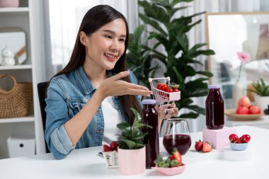 Gülümseyen, güzel Asyalı genç, lezzetli karışık çilek ve kiraz suyu detoksu içeceklerini inceleyen, sosyal medyada özel promosyon satışı için sağlıklı ürünler sergileyen. Taktik.