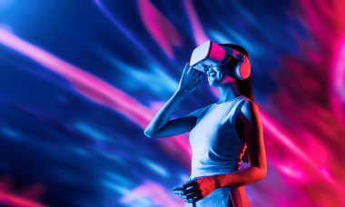 Zeki bir kadın, metaevreni birbirine bağlayan VR kulaklık takan neon ışıklarla çevrili duruyor. Gelecekteki siber uzay topluluğu teknolojisi. Uzaklara bakan zarif bir kadın ve tatmin edici bir şekilde gülümsüyor. Halüsinasyon.