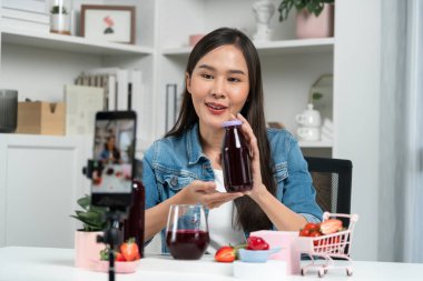 Gülümseyen, güzel Asyalı genç, lezzetli karışık çilek ve kiraz suyu detoksu içeceklerini inceleyen, sosyal medyada özel promosyon satışı için sağlıklı ürünler sergileyen. Taktik.