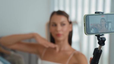 Genç sosyal medyum kadın moda videosu yapıyor. Blogcu kameraya selfie çubuğu ve ışık halkası kullanarak gülümserken, aynı zamanda ikna edici çevrimiçi kıyafetlerin izleyicilere veya takipçilere vlog satmasını sağlıyor. Düzenle