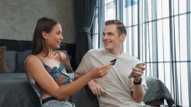 Genç çift, kredi kartıyla ödemek için internet üzerinden ödeme uygulaması ve dijital cüzdan kullanarak yatak odasında oturuyor. Mobil internet üzerinden alışveriş ve modern alımlar. Düzenle
