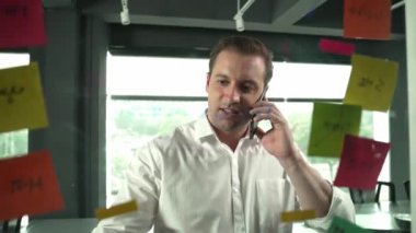 Profesyonel işadamı renkli yapışkan notlara yazılmış pazarlama stratejisi fikrine bakarken müşterilerine telefon ediyor. Proje yöneticisi duvardaki telefon analiz verileriyle konuşuyor. Yönlendirici.