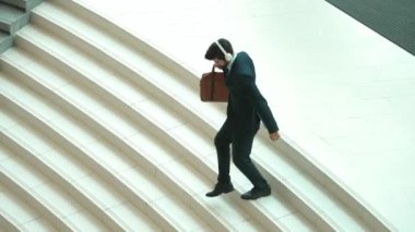 Merdivenlerden inerken kulaklıktan müzik dinleyen mutlu bir iş adamı. Yönetici, satışların artmasını, başarılı projeleri veya yeni pozisyonları kutlamak için dans ediyor. Sevinçli..