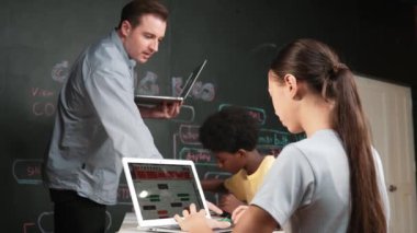 Afrikalı erkek manken tamir ederken beyaz kız programlama ya da kodlama sistemi. Öğretmen elinde dizüstü bilgisayar tutarken çeşitli çocukların web geliştirme programı yazmalarına bakıyor. Yenilik eğitimi. Öğretim