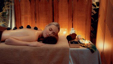 Lüks tatil köyündeki kaplıcalarda sıcak taş masajı, sıcak mum ışığı, spa bazalt taşı masajının keyfini çıkaran mutlu kadın müşteriler, rahatlatıcı bir sıcaklıkla vücudun üzerinde süzülüyorlar. Sessiz.