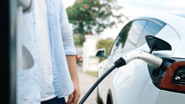 Modern çevre dostu adam EV şarj istasyonundan elektrikli aracı şarj ediyor. EV araba teknolojisi ev sakinleri için gelecekte çevresel sürdürülebilirlik için kullanılıyor. Eşzamanlama