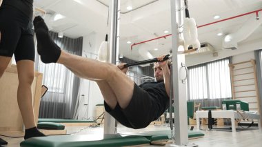 Profesyonel pilates eğitmeni, bir müşteriye jimnastik salonunda pilates yaparken rehberlik ediyor. Çekirdek dengesini ve omurilik hizasını iyileştirmek için çubuğa tutunan bir adam. Sağlıklı olmak. Alışkanlık.
