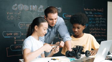 Kafkas öğretmen dizüstü bilgisayara bakarken araba modelleme sistemini kara tahtada kodlama veya programlama koduyla açıklıyor. Robot inşaatını öğrenen çeşitli öğrencileriniz kutlu olsun. Öğretim.