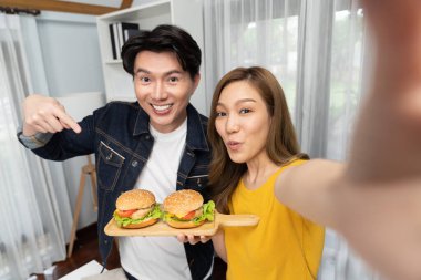 Gülümseyen sunucu şefler akıllı telefonlarıyla fotoğraf çekiyorlar. Özçekim yoluyla. Yemek programında çift hamburger tutuyorlar. İnfobahn.