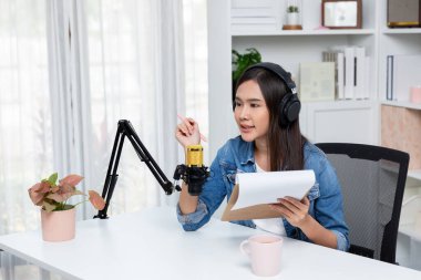 Sosyal medyada kulaklıkla canlı yayın yapan Asyalı sunucu modern stüdyoda yaşam koçluğu veya pazarlama dinleyicilerini selamlıyor. Taktik.