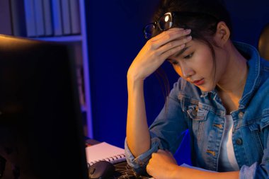 Stresli, genç, güzel Asyalı yaratıcı proje yaratıcısı sosyal medyayı araştırmak için bilgisayara bakıyor ve geceleri daha çok neon modern ofisin planlama kanalı stratejisine ulaşılıyor. Taktik.