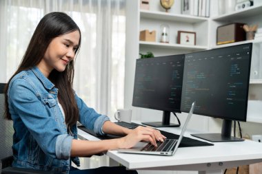 IT geliştiricisinde gülümseyen genç Asyalı dizüstü bilgisayarında kodlama programı verileriyle kotlu tişört giyerek çevrimiçi bilgi yazıyor. Güvenlik analizi iki ekran ile çevrili. Taktik.