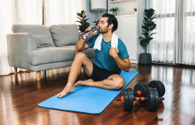 Atletik ve sporcu adam spor paspası üzerinde su içiyor. Vücut egzersizlerini bitirdikten sonra evdeki formda ve sağlıklı spor yaşam tarzı için egzersiz yapıyor. Gaiety evde egzersiz eğitimi.