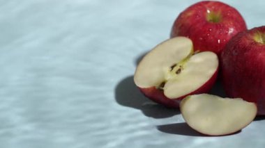 Mavi arka planda dilimlenmiş kırmızı elmaları kapatın. Elma dilimlenmiş makarnanın mavi arka planında elmacı ve suyun dökülmesi ve el sallaması. Sağlıklı beslenme ve taze üretim kavramı. Pabulum.