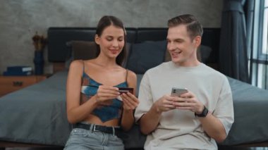 Genç çift, kredi kartıyla ödemek için internet üzerinden ödeme uygulaması ve dijital cüzdan kullanarak yatak odasında oturuyor. Mobil internet üzerinden alışveriş ve modern alımlar. Düzenle