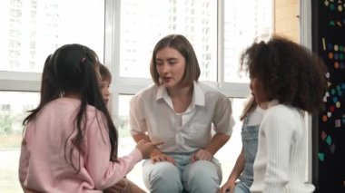 Genç öğretmen dikkatle dinlerken Asyalı öğrenci hikaye anlatıyor. Etrafı çeşitli arkadaşlarla çevrili şirin bir kız birbirini önemsemeyi ya da anlamayı öğreniyor. Yaratıcılık eğitimi konsepti. Etkinlik.