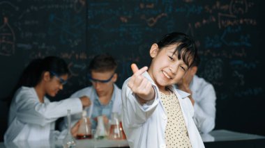 Asyalı bilim adamı çeşitli gruplar deney yaparken minyatür kalbi kameraya gösterdi. Laboratuvarda laboratuvar önlüğü giyerken yazılı kimyasal teorisiyle tahtada duran genç bir öğrenci. Öğretim.