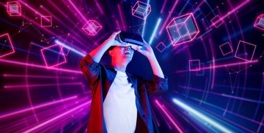 Afrikalı adam, VR kulaklık takıp parlak mavi ve pembe geometrik şekillerde dururken metaevreni keşfetmek için heyecanlanıyor. Oyuncu artırılmış gerçeklik gözlüğü kullanırken oyun oynuyor. Yaratıcılık.