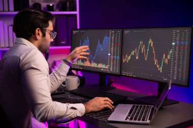 Akıllı tüccar işadamı, karanlık oda gecesinde neon ışıklı ofisteki arama pazarında yüksek kârla ekranda bilgisayar ve bilgisayar üzerinde dinamik borsa yatırımları üzerinde yoğunlaşıyor. Tahmin et..