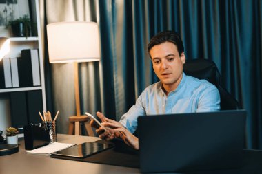 Akıllı iş adamı, müşterilerle veya yatırımcılarla iletişim kurmak için akıllı telefonuyla çalışır. Laptop ve tablet veritabanında geceleri mavi perde arkasında iş hedefiyle birlikte araştırma yapar. Bireysel.