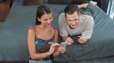 Genç çift, kredi kartıyla ödemek için internet üzerinden ödeme uygulaması ve dijital cüzdan kullanarak yatak odasında oturuyor. Mobil internet üzerinden alışveriş ve modern alımlar. Düzenle