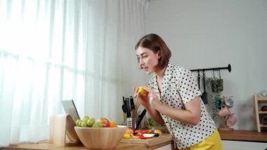 Kafkasyalı anne, modern mutfakta dizüstü bilgisayarda yemek tarifine bakarken salata yapmak için yemek hazırlıyor. Yetenekli ev bekçisi taze sebze kullanarak kahvaltı hazırlıyor. Pedagoji.