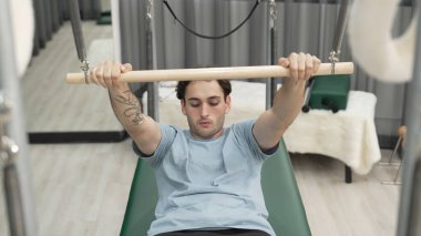 Adam spor salonundaki kol ve vücut kaslarını güçlendirmek için pilates trapez çubuğunda çekirdek egzersizi yapıyor. Göğüs ve omuz güçlendirmek için Cadillac 'a göğüs presi yapan antrenör. Alışkanlık.