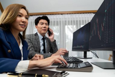 Gülümseyen Asyalı işadamı komisyoncu dinamik borsa veritabanını arıyor. Kadın iş ortağı, iç işyerindeki kar eden uygulama programını karşılaştıran ekranlara işaret ediyor. İnfobahn.