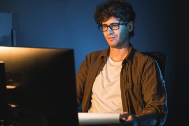 Genç işadamı, Neon Light Modern Ofis 'teki yeni proje surround çalışma masası için kağıt üzerinde tasarım düşünüyor. E-posta ile hediye göndermeden önce not defterine yeni bir iş düşünüyorum. Toplayıcı.