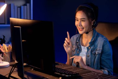 Sunucu kanalı Asyalı etkileyicisi canlı yayında konuşuyor. Sosyal medyada kulaklık takıyor, bilgisayar kaydı yapıyor, dinleyicileri selamlıyor ve Neon Modern Stüdyoları 'nda online olarak koçluk yapıyor. Taktik.