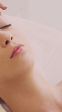 Lüks bir spa merkezinde masaj terapisti tarafından yüz masajı ve spa tedavisi için kaplıcaya uzanmış rahat bir kadın. Sağlık, stres atma ve gençleştirme kavramı.