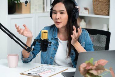 Sosyal medyada kulaklıkla canlı yayın yapan Asyalı sunucu modern stüdyoda yaşam koçluğu veya pazarlama dinleyicilerini selamlıyor. Taktik.