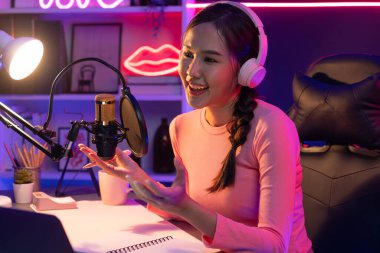 Geceleri podcast 'te olumlu konuşmalar yapan, pembe neon ışıklı modern stüdyoda sunum için dizüstü bilgisayar kullanan, gülümseyen, genç, güzel Asyalı bir etkileyiciydi. Taktik.