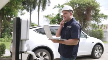 Evde EV şarj istasyonu kurulumu üzerinde çalışan nitelikli teknisyen, EV için dizüstü bilgisayarla şarj sisteminde sorun çıkarma ve yapılandırma ayarları yapıyor. Titiz