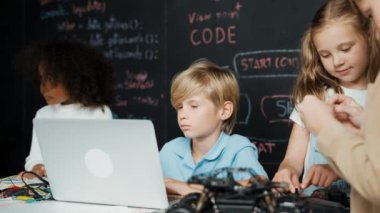 Çocuğun dizüstü bilgisayar mühendisliği kodunu ve yazım programını kullanırken bir grup zeki öğrencinin etrafı STEM teknoloji sınıfında arkadaşlarıyla çevriliyken karatahtaya oturması. Etkinlik.