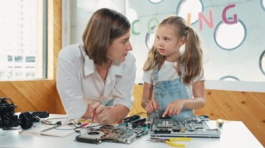 Genç, zeki, beyaz bir öğretmen öğrencilere elektronik kurulun bir parçasını öğretiyor. Uzman kız dijital elektrikli aletleri öğreniyor ve cips ve kablolarla ana kartı tamir ediyor. Etkinlik.